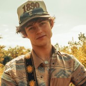 A man wearing a western printed shirt, cap, and sunglasses